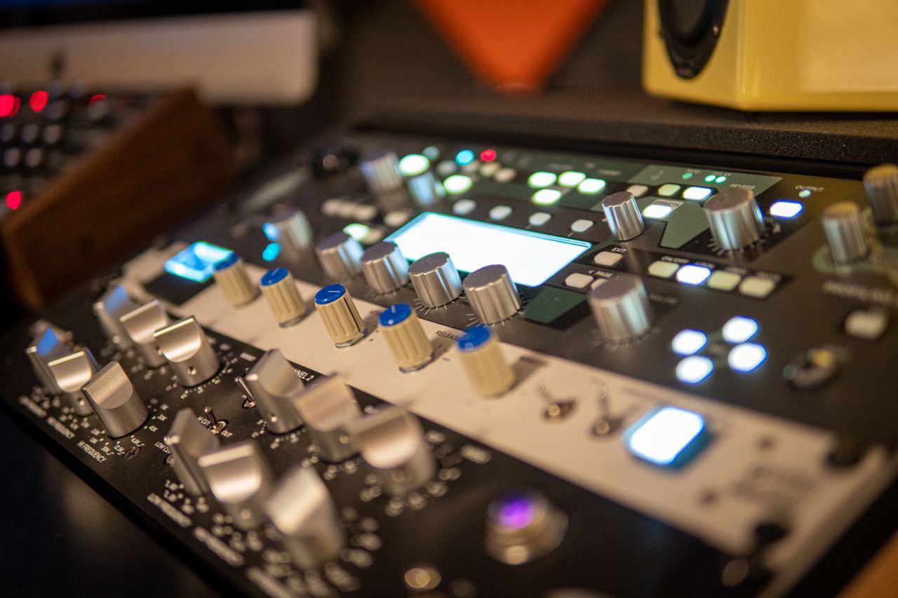 Close-up of a professional audio mixer with knobs and lights in a modern recording studio setting.